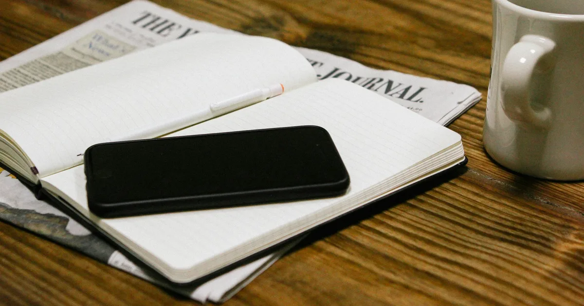 Notes being read on a phone beside coffee at a desk