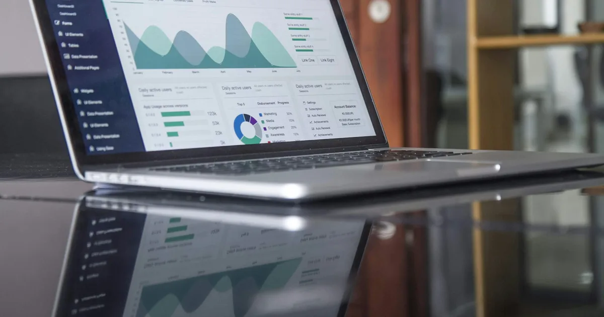 A laptop showing a spreadsheet being compared on a desk